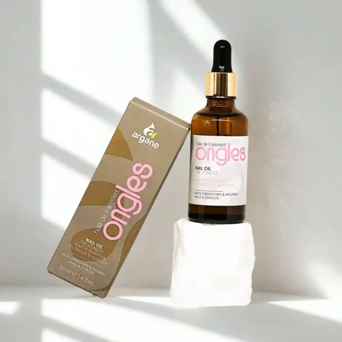 Gydomasis aliejus nagams stiklo buteliuke su dozatoriumi, šalia pakuotės, ant balto akmens.