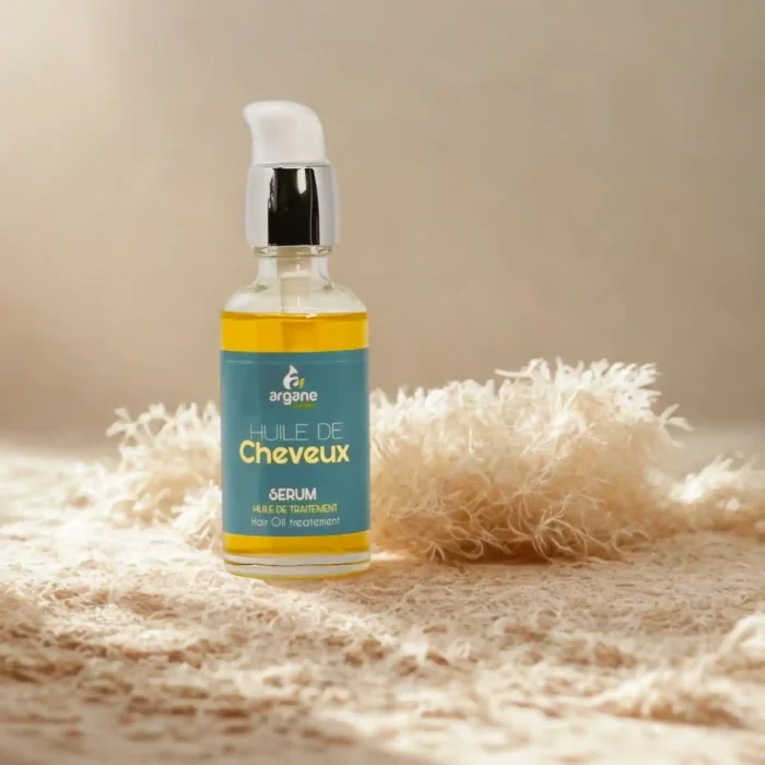 Gydomasis serumas plaukams skaidriame buteliuke su dozatoriumi ant smėlio spalvos paviršiaus.