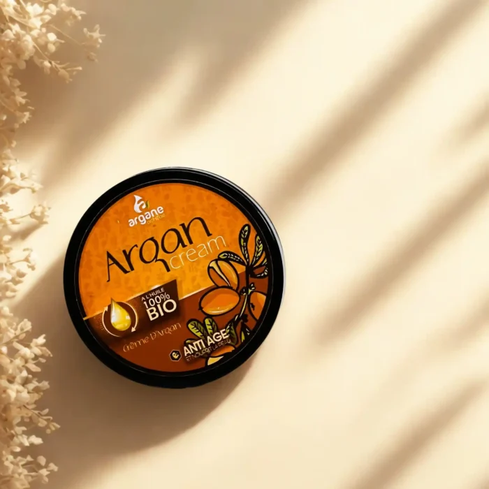 Ekologiškas argano aliejaus kremas veidui nuo senėjimo (Anti Age) tamsioje pakuotėje, ant šviesaus paviršiaus su šešėliais.