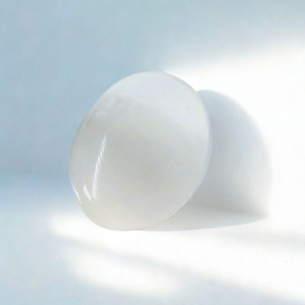 Baltas skaidrus selenito delninukas (palm stone) nuo streso ir nerimo, minimalistiniame fone