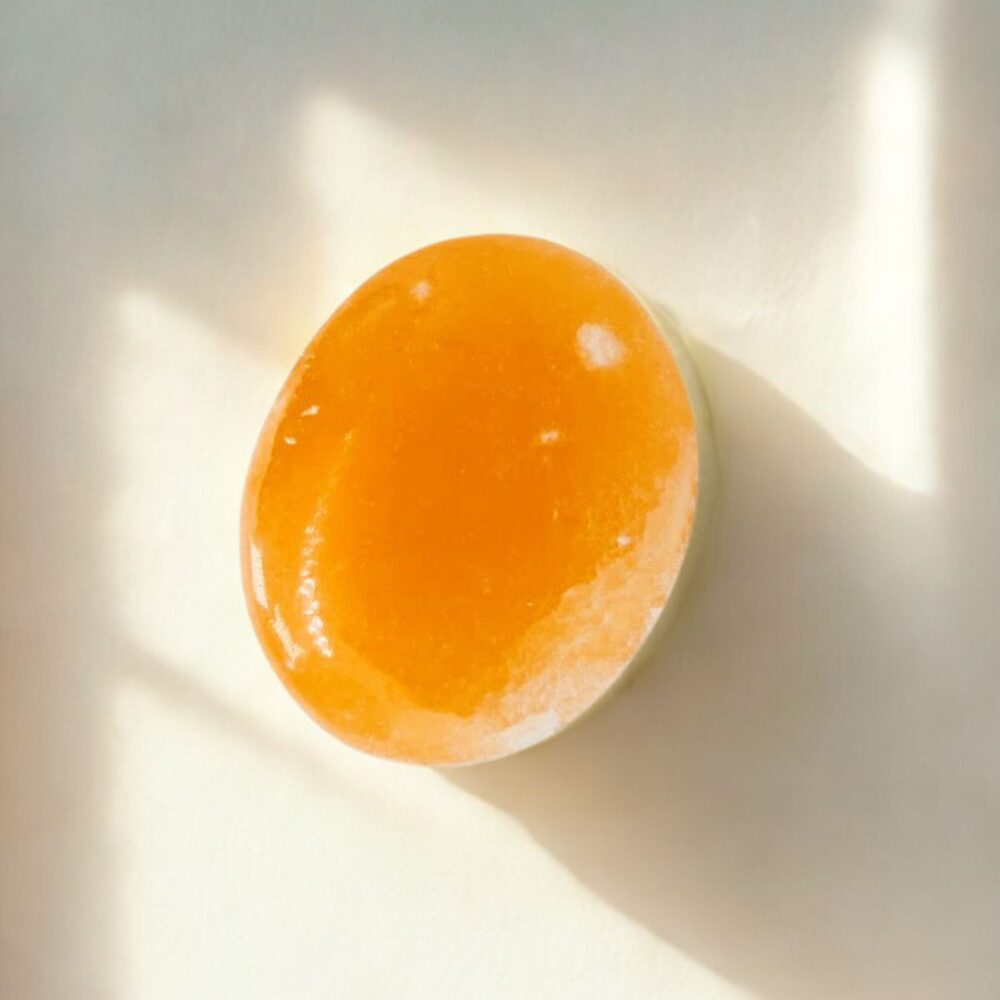 Oranžinis selenito delninukas (palm stone) nuo streso, minimalistiniame fone