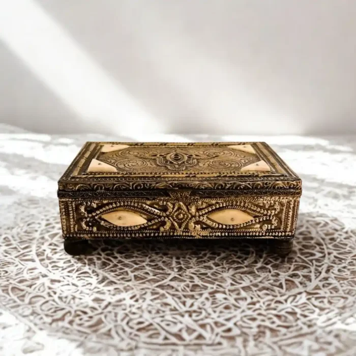 Medinos paslapčių dėžutė - metalinė, dekoruota raižiniais ir kaulo intarpais, ant ažūrinės staltiesės.