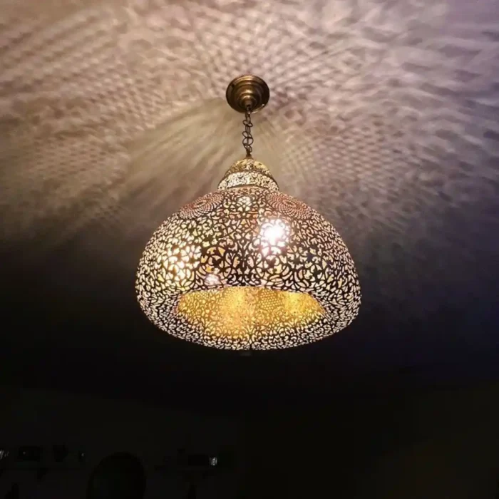 Rankų darbo įjungtas marokietiškas žalvario šviestuvas, skleidžiantis sudėtingus arabeskų raštus ant lubų.