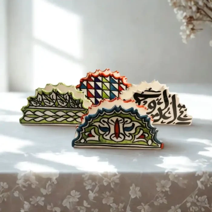 Keturi rankų darbo keraminiai spalvingi marokietiški servetėlių laikikliai ant balto, nėriniuoto užtiesalo.Keturi rankų darbo keraminiai spalvingi marokietiški servetėlių laikikliai ant balto, nėriniuoto užtiesalo.