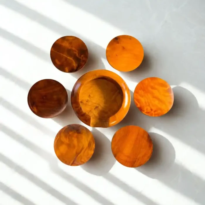 Šeši apvalūs mediniai padėkliukai puodeliams dėklu, išdėstyti ant šviesaus paviršiaus ryškioje šviesoje.