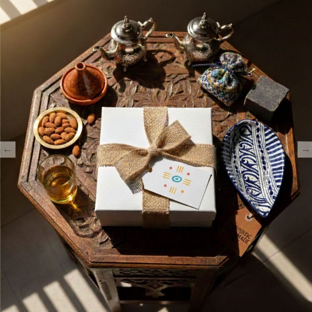 Dovana baltoje dėžutėje su kaspinu ant raižyto medinio staliuko šalia marokietisku ranku darbo arbatinuku ir keramikos